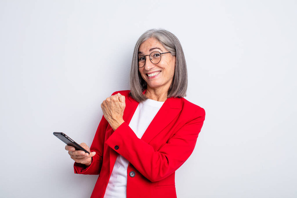 senior pretty woman feeling happy and facing a challenge or celebrating.. business and phone concept - 写真・画像