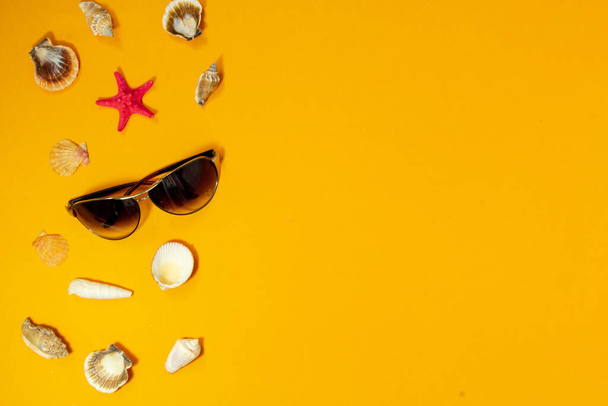 Top view tropical summer background. Sunglasses with starfish, seashells on a yellow background. summer travel concept. Flat lay with copy space. - Foto, imagen