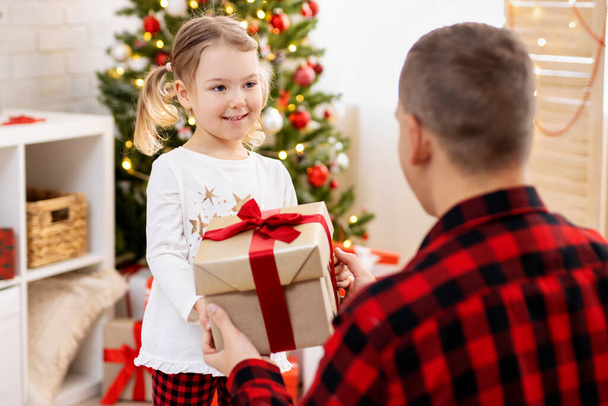 Батько дарує подарунок своїй щасливій дочці в різдвяній прикрашеній вітальні
 - Фото, зображення