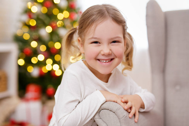 Nahaufnahme Porträt eines glücklichen kleinen Mädchens in der Nähe des Weihnachtsbaums - Foto, Bild