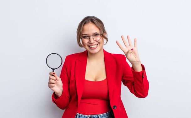 hispanic pretty woman smiling and looking friendly, showing number four. magnifying glass concept - Foto, Imagen