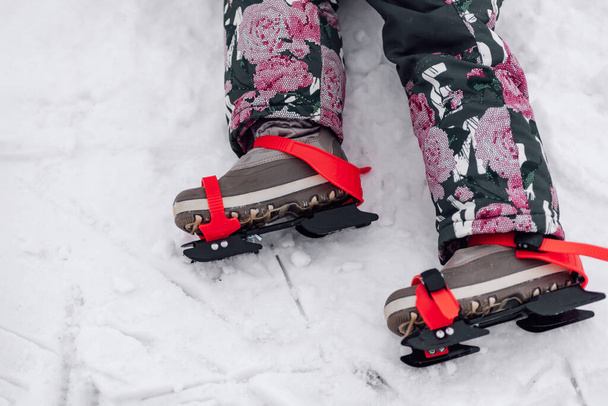 Children skates. Close-up of children ice skates tied to winter boots with red ribbons, side view, snow background - Fotoğraf, Görsel