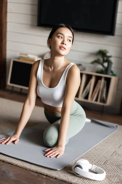 Menina asiática fazendo ioga alongamento em casa, treino em sua sala de estar, vestindo activewear - Foto, Imagem