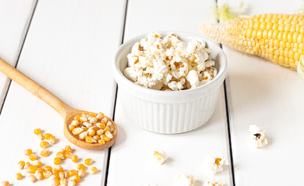 Popcorn, kolba kukurydzy i ziarna kukurydzy, widok z góry na białym drewnianym tle - Zdjęcie, obraz
