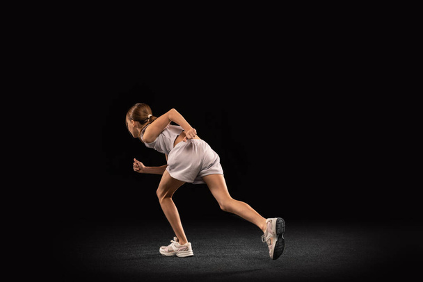 Full-length portrait of girl, teenager, professional runner training isolated over black background - 写真・画像