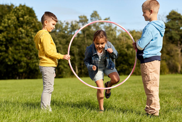happy children playing game with hula hoop at park - Фото, изображение