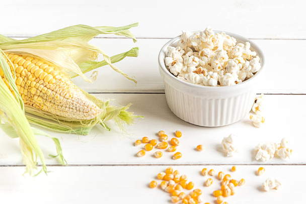 Popcorn, maïskolf en maïskorrels, bovenaanzicht op een witte houten ondergrond - Foto, afbeelding