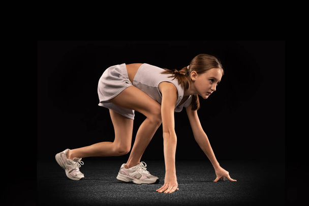 Genç bir kızın tam boy portresi, koşan bir sporcu siyah arka planda tek başına koşmaya hazırlanıyor. - Fotoğraf, Görsel