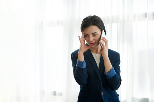 Atrakcyjna brunetka, pracownica, zmęczona bizneswoman kładąca rękę na skroni podczas nudnej rozmowy przez telefon - Zdjęcie, obraz