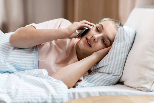 happy girl calling on smartphone in bed at home - Fotó, kép