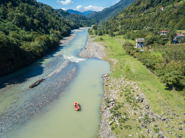 Drone vista de un barco navegando a lo largo de un río de montaña entre las montañas en un día soleado en Georgia - Foto, imagen