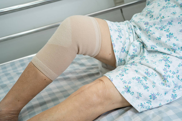 Aziatische senior of oudere oude dame patiënt met knie ondersteuning pijn gewricht op bed in verpleegkundige ziekenhuis afdeling, gezonde sterke medische concept. - Foto, afbeelding