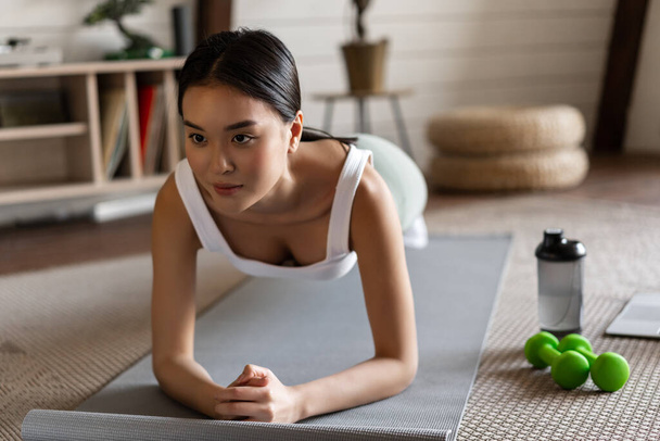 Sporty asian girl in activewear doing workout at home, follow video sport guide, online fitness instructor on laptop, standing in plank on floor mat - Foto, Imagem