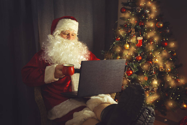Authentic Santa Claus is working on a laptop. Home interior. In anticipation of Christmas and New Years.  - Zdjęcie, obraz