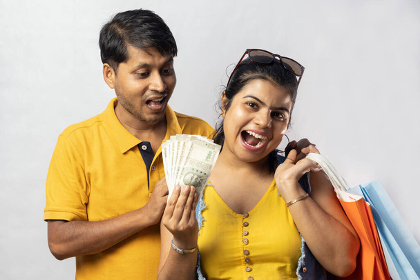 Pareja india en vestido amarillo con bolsas de compras y grandes ahorros sonriendo sobre fondo blanco - Foto, imagen