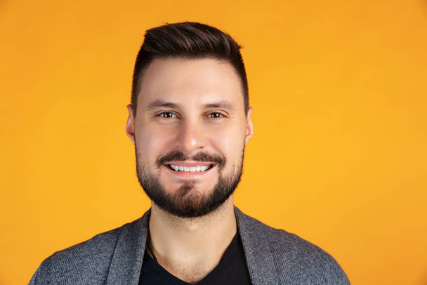 Cropped portrait of emotive man, smiling and looking at camera, posing isolated over yellow background - Fotografie, Obrázek