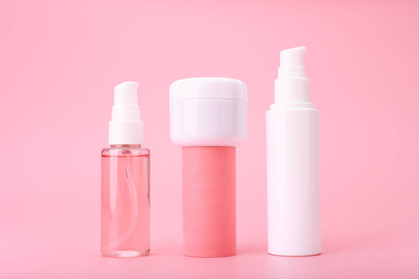 Set of beauty products in a row on white table against pink background. Face cleansing foam, cream and lotion - Photo, image