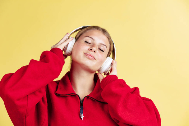 Young smiling beautiful girl listening to music with closed eyes isolated on yellow studio background. Concept of emotions, - Foto, Bild