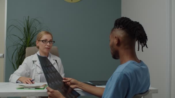 Άνδρας ασθενής που κοιτάζει την εικόνα της μαγνητικής τομογραφίας, ανακρίνει γυναίκα γιατρό μέσα - Πλάνα, βίντεο