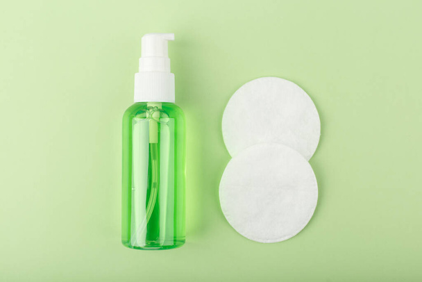 Zblízka kůže čisticí pěna nebo gel vedle dvou bavlněných podložek na světle zeleném pozadí - Fotografie, Obrázek