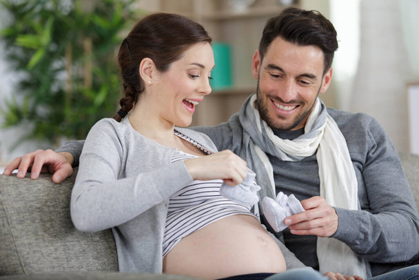 pregnant woman and her husband holding baby booties on bump - Foto, Bild