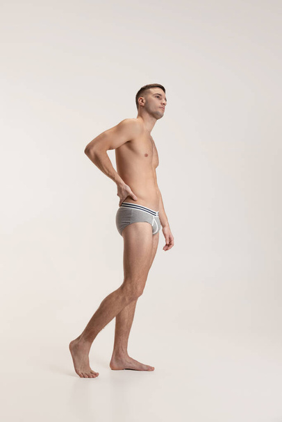 Studio shot of young handsome sportive shirtless man in underwear standing isolated on grey studio background. - Foto, immagini