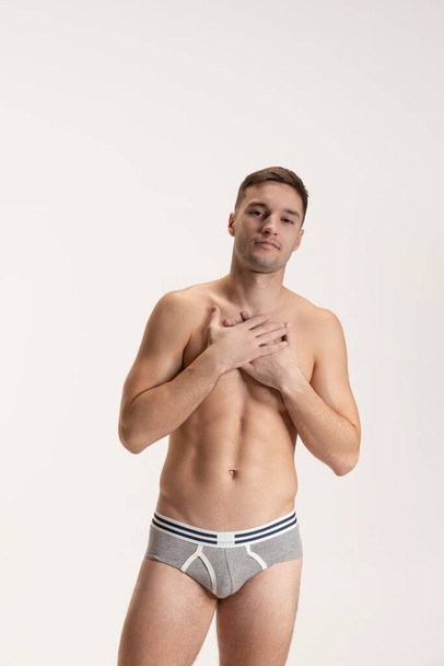 Studio shot of young handsome sportive shirtless man in underwear standing isolated on grey studio background. - Foto, afbeelding