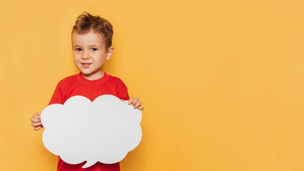 Студійний портрет щасливого хлопчика з чистою білою дошкою у формі хмари на яскраво-жовтому тлі, з місцем для тексту або реклами
 - Фото, зображення