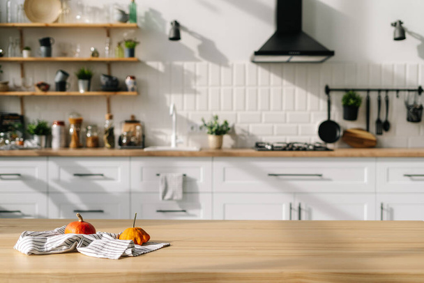 Moderne stijl keuken interieur met kleine pompoenen op handdoek. Hedendaagse witte meubels, bestek, planten, apparaten en decor op achtergrond - Foto, afbeelding