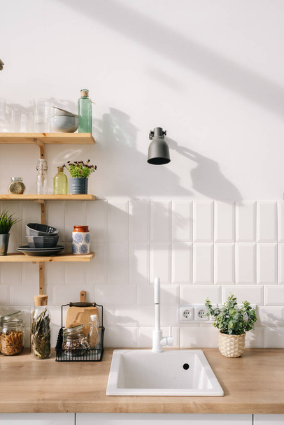 Fregadero moderno encaja perfectamente en el diseño interior de la cocina escandinava en tonos blancos. Concepto de muebles y estantes de madera. Apartamento de lujo en alquiler - Foto, imagen
