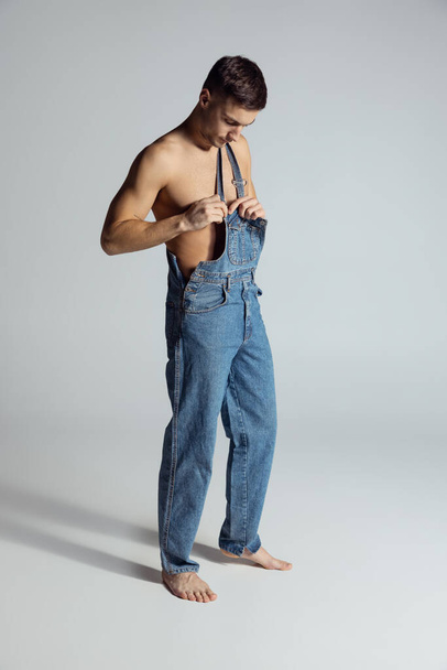 Portrait of young handsome sportive shirtless man in jeans posing isolated on gray studio background. - 写真・画像