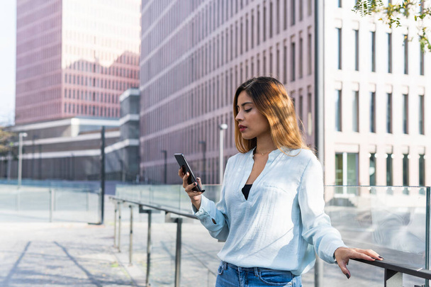 Business latin woman is having a business discussion through the phone surrounded by buildings. Business concept - Photo, Image