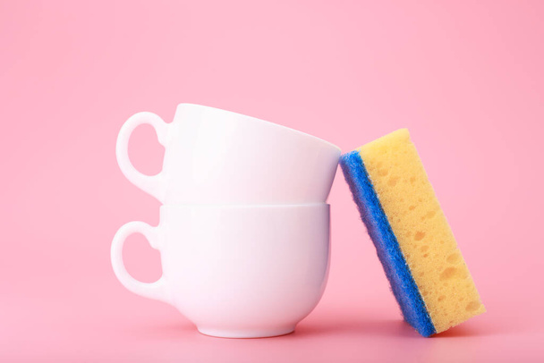 Creative, minimal dishwashing concept, yellow cleaning sponge next to two white ceramic cups on pink background - 写真・画像