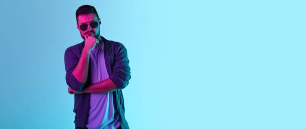 Cropped portrait of brutal bearded man in sunglasses posing isolated over blue background in neon lights - Foto, Bild