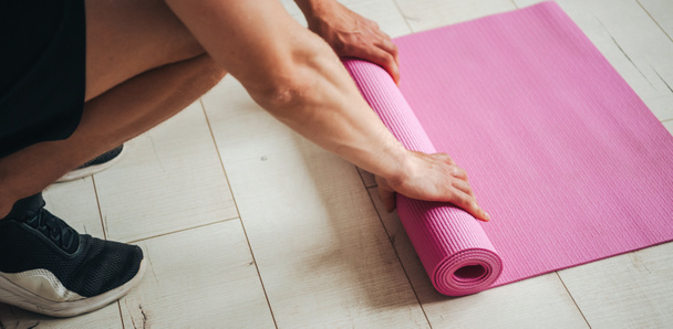 Close portrait of mans hands unrolling exercise mat while preparing for workout at home. Healthy lifestyle. - Photo, Image