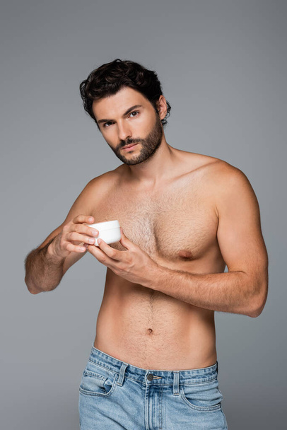 shirtless man holding container with cosmetic cream isolated on grey  - Fotó, kép