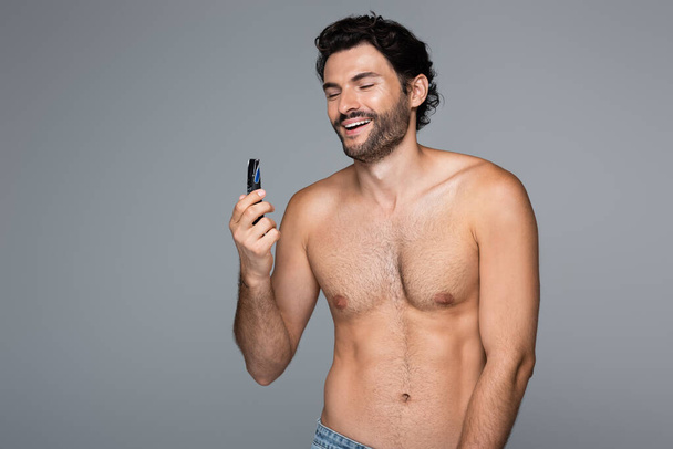 bearded and happy man holding electric razor isolated on grey - Fotó, kép