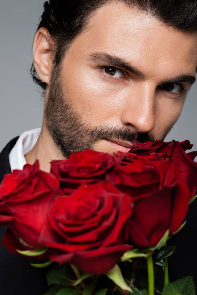 close up of bearded man holding bouquet of red roses isolated on grey - Photo, image