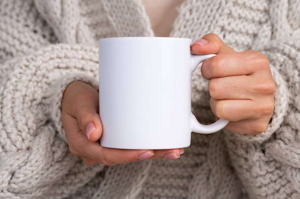Woman in knitted sweater holding white mug in hands. Winter cup Mockup for Christmas individual gifts design - Φωτογραφία, εικόνα