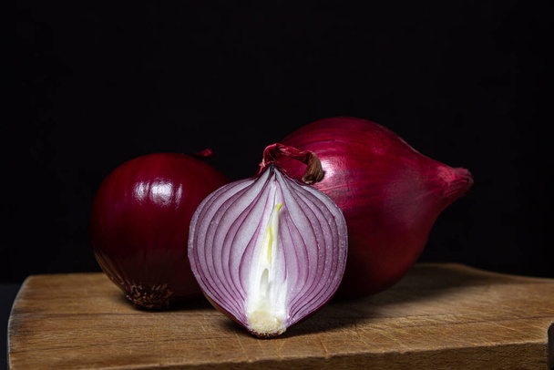Red onion on a black background. Red onion cut in half on a board. Onion variety - Foto, Imagen