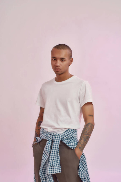 Cool stylish young mixed race man in casual street wear looking at camera, standing isolated over pink studio background - Fotó, kép