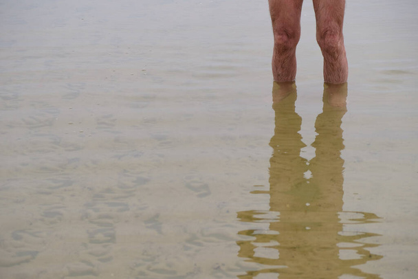 Reflejo borroso de un hombre en agua clara en un día de niebla. Pies peludos húmedos sobre fondo de agua. Copiar espacio. - Foto, imagen