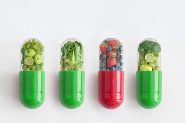 Red vitamin capsule containing antioxidant berries standing out amongst green pills  - Fotó, kép