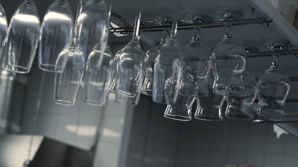 Крупним планом окуляри висять догори ногами в ресторані кухні. HDR. Багато чистих прозорих келихів для вина та коктейлів на білих стінах та стельовому фоні
. - Фото, зображення