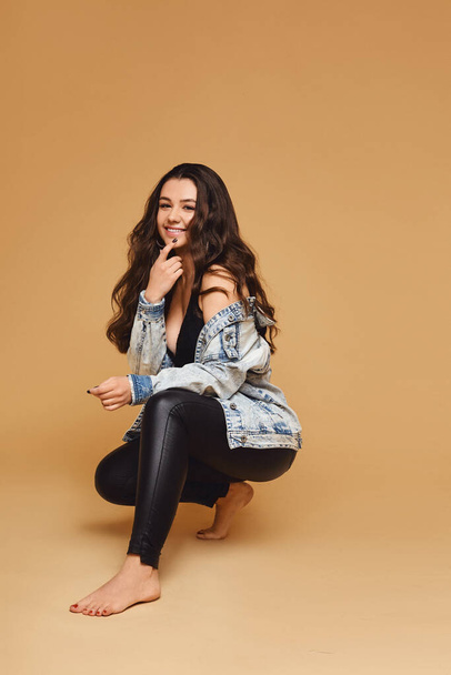 Happy attractive young woman in leggings and denim jacket over beige background - Valokuva, kuva