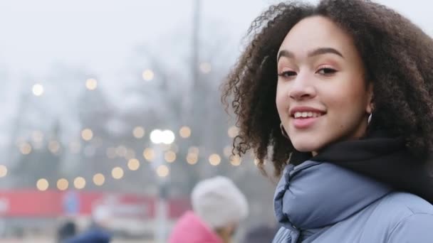Close-up portrait african american curly beautiful young woman looks at city standing in profile side view girl female student mixed race teen lady standing outside outdoors looking at camera smiling - Footage, Video