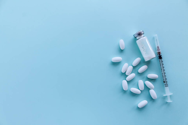 Egy üveg fehér por, egy fecskendő és egy csomó fehér tabletta, szürke-kék háttérrel a jobb oldalon, felülnézetből. - Fotó, kép