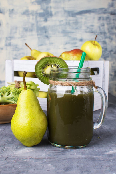 Green smoothie in a glass next to a box of fruits on a gray table. - Photo, Image
