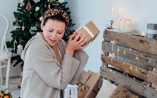 Beautiful young woman receiving a wrapped Christmas gift. Giving a present in cozy christmas decorated interior. - Photo, image