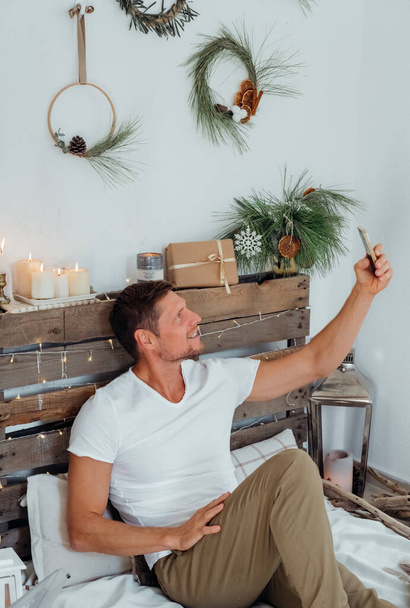 Hombre feliz tomando fotos en el móvil en casa decorada navidad. Familia felicitaciones en línea. - Foto, Imagen